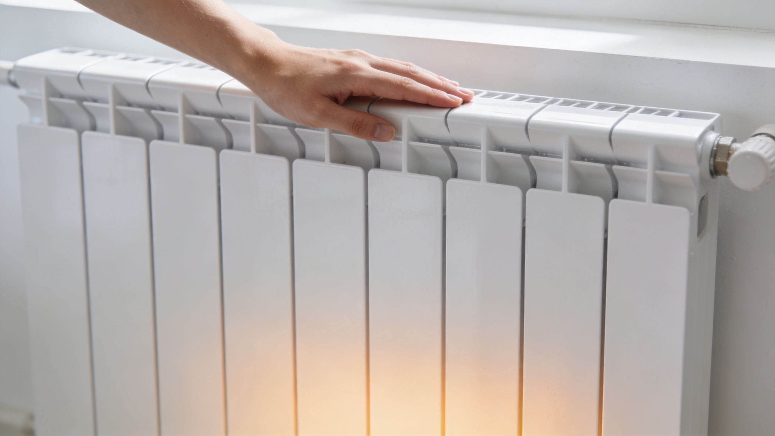 En person lægger en hånd på en hvid radiator for at mærke varmen i hjemmet.