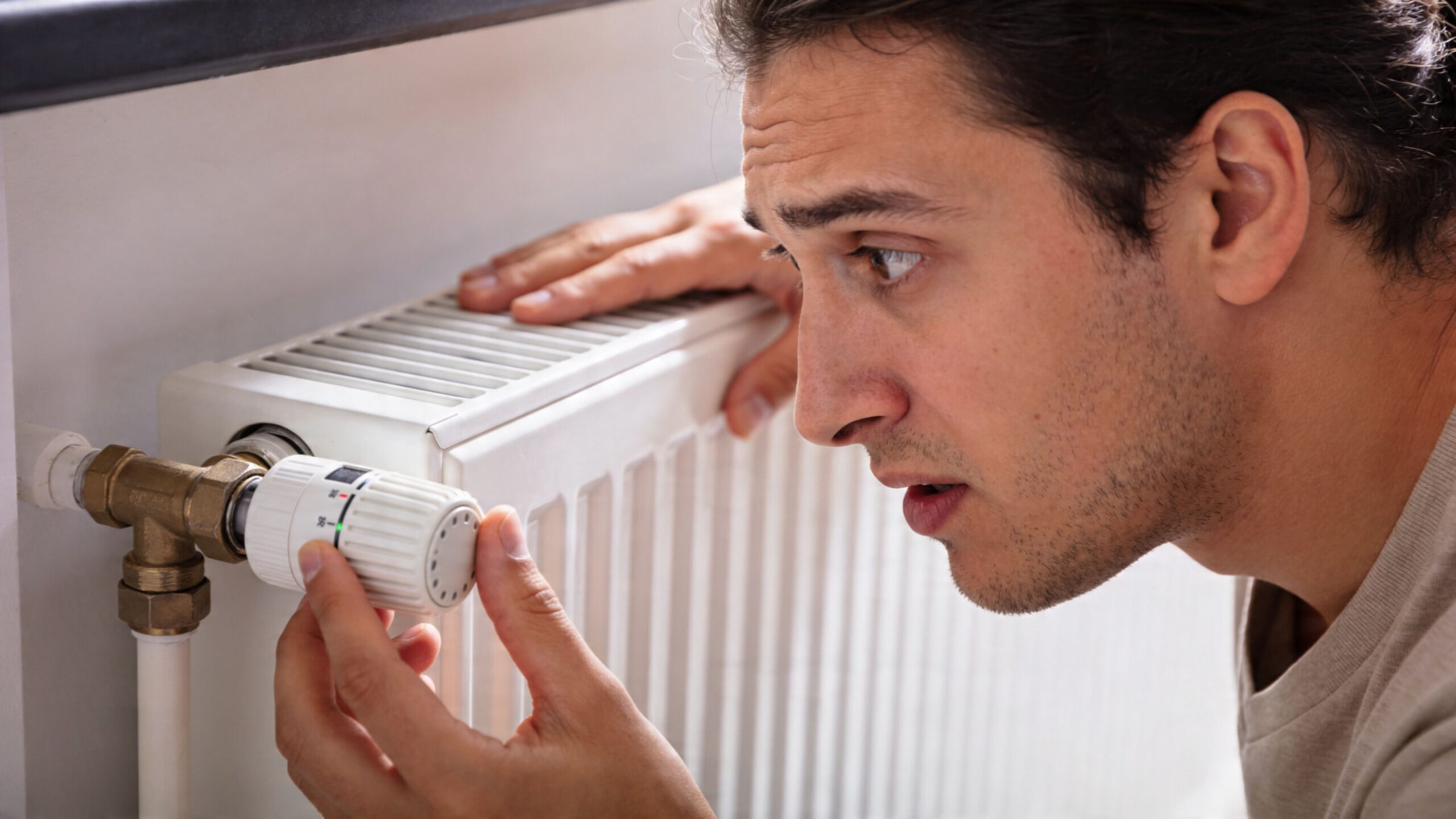 En mand ser forvirret på en radiatortermostat, mens han prøver at justere den derhjemme.