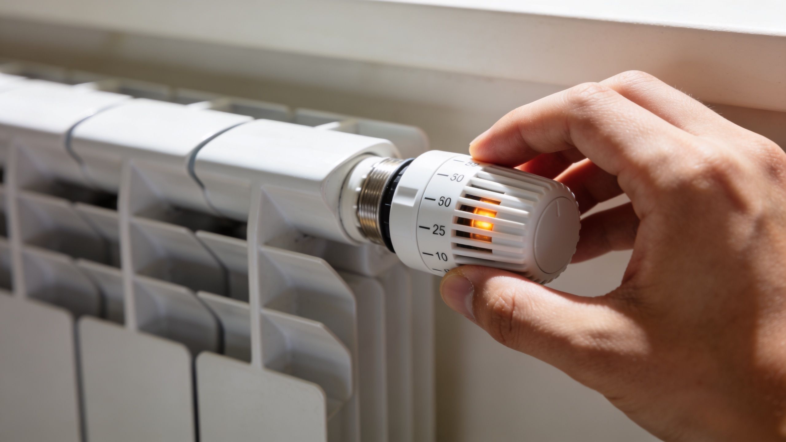 En hånd der justerer termostaten på en hvid radiator for at styre rummets varme og temperatur.