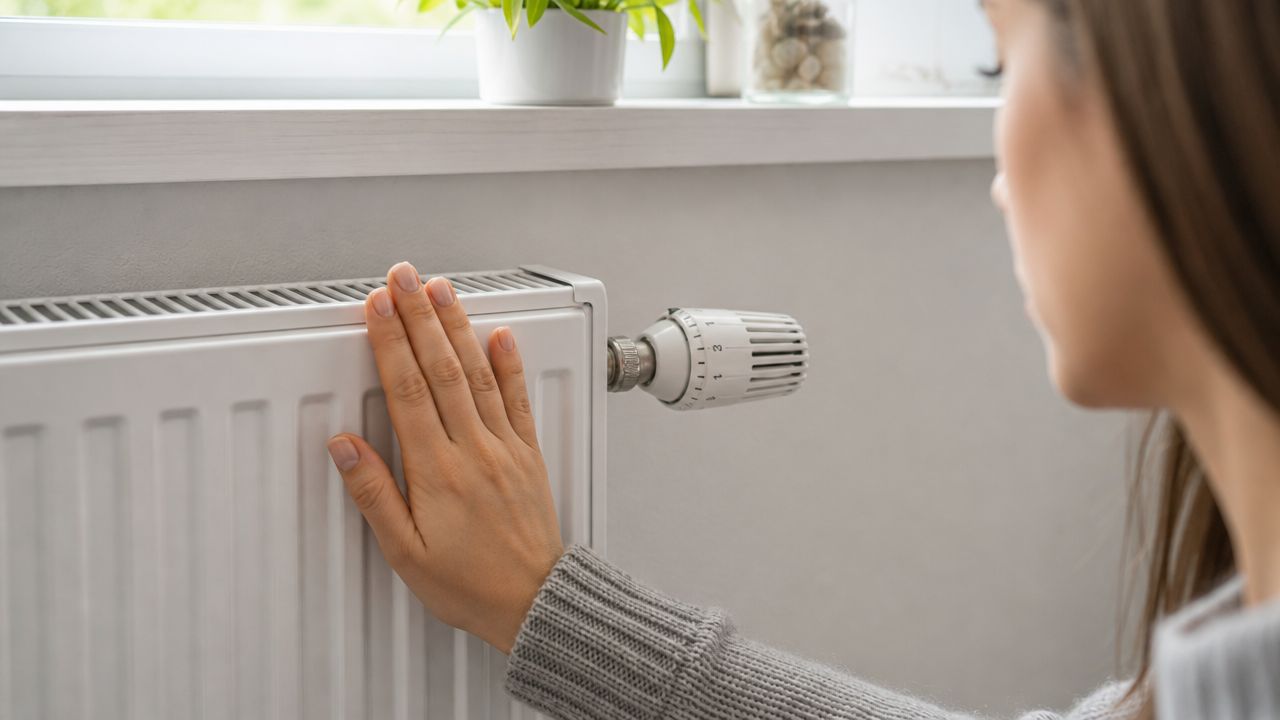 En kvinde mærker på en hvid radiator med hånden for at tjekke, om den bliver varm.