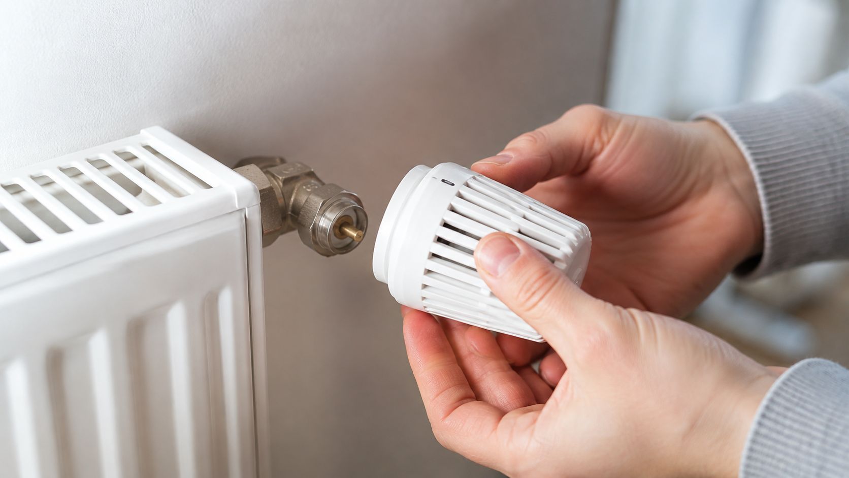 En person monterer en ny termostat på en radiator for at justere varmen i hjemmet.